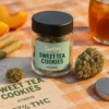 Hand holding child-resistant Moonrock jar against blurred laptop showing order confirmation screen, shipping box visible. Logo embossed on jar base.