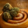 Berner Cookies Sticky Buns - Bakery-Fresh Cannabis Strain | Moonrock Berner Cookies Sticky Buns cannabis nugs on cinnamon roll with Moonrock Online Shop hologram