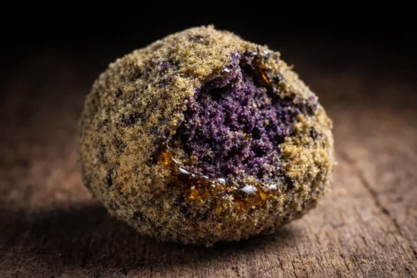 Single purple moonrock nug coated in oil and kief with a cracked edge showing dark purple interior on a raw wood surface