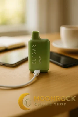 Elf Bar BC5000 disposable vape charging via USB-C on a desk with phone and coffee, Moonrock Online Shop logo watermark