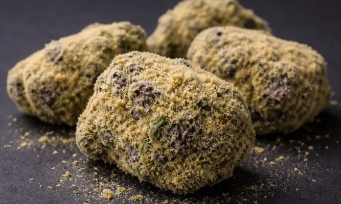 Close up of dense cannabis moonrocks heavily coated in golden kief showing infused bud texture