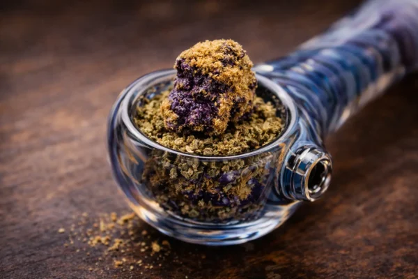 Small piece of purple moon rocks bud placed on top of ground flower in a clean glass pipe bowl