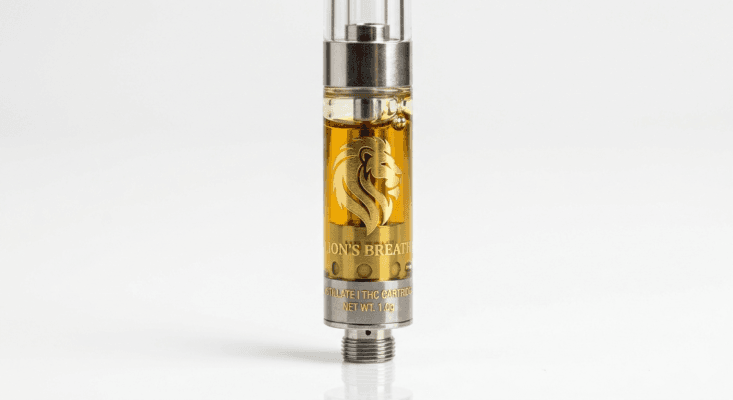 A close-up, professional studio photograph of a Lion's Breath THC vape cartridge standing upright against a clean white background. The cartridge is filled with clear, golden-amber distillate and features a prominent gold lion logo etched into the glass. The metallic hardware at the top and bottom is polished silver, with "LION'S BREATH" and "NET WT. 1.0g" visible in gold lettering.